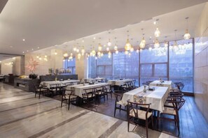 A spacious restaurant with multiple dining tables and chairs, large windows, and hanging light fixtures. - Jing Jiang Hotel (Lianjiang)