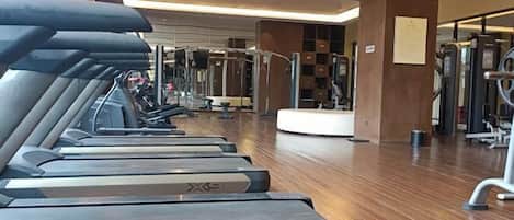 A gym with treadmills, weight machines, and a wooden floor.