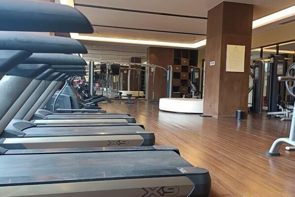 Une salle de sport équipée de tapis de course, d’appareils de musculation et dotée d’un plancher en bois.