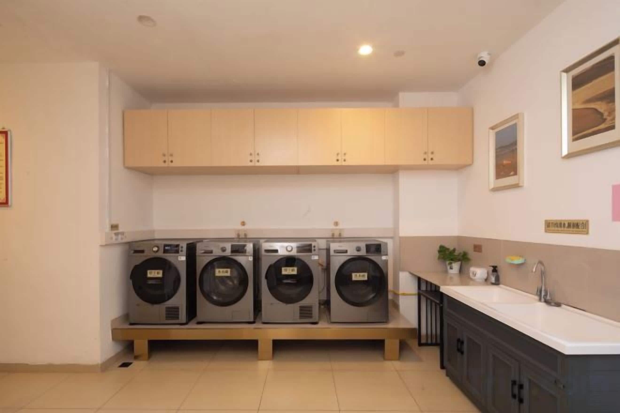 A laundry area with four washing machines, a sink, and wooden cabinets.