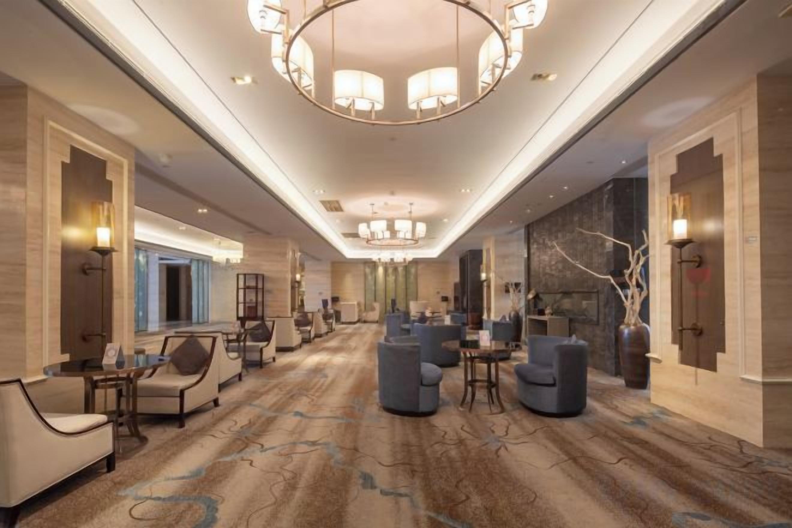 A spacious hotel lobby with a central seating area, a chandelier, and a carpeted floor.