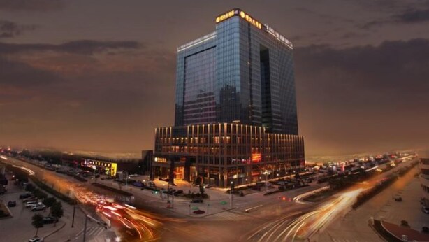 A modern high-rise hotel with a prominent glass facade and illuminated signage. - Jing Jiang Hotel (Lianjiang)