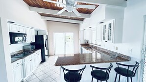 A modern kitchen with white cabinets, a granite countertop, and a central island with bar stools. - Blue Bird Villa, Open & Breezy Island Home...minutes from the beach! (Providenciales)