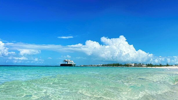 A clear view of a boat on turquoise water with a beach and buildings in the background. - Blue Bird Villa, Open & Breezy Island Home...minutes from the beach! (Providenciales)