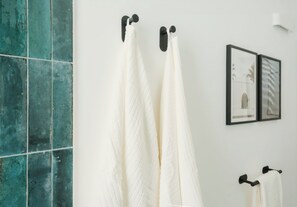 Une salle de bain avec un mur carrelé, deux serviettes suspendues à des crochets et deux tableaux encadrés accrochés au mur.