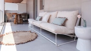 A modern outdoor seating area with a white sofa, a round woven rug, and a dining table with chairs.