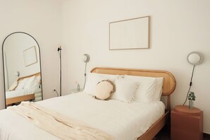 Un lit bien fait, avec du linge de lit blanc, une tête de lit en rotin et deux lampes de chevet.