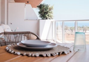 Un coin repas avec une table dressée pour deux personnes, une chaise en osier et une vue sur la mer.