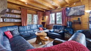 A cozy cabin interior with a large blue leather sofa, a wooden coffee table, and a bookshelf filled with books. - Spacious chalet in La Rosière with hammam and jacuzzi for 15 people (Montvalezan-La Rosière)