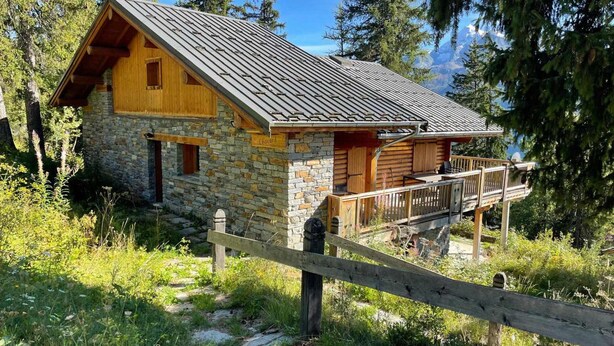 A stone cabin with a wooden deck and a metal roof, surrounded by trees and a clear sky. - Spacious chalet in La Rosière with hammam and jacuzzi for 15 people (Montvalezan-La Rosière)