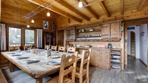A wooden cabin interior with a dining table set for four, wooden chairs, a kitchen area with shelves, and a large window. - Spacious chalet in La Rosière with hammam and jacuzzi for 15 people (Montvalezan-La Rosière)