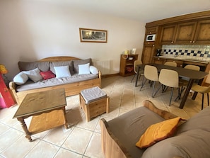 Een woonkamer met een bank, een salontafel, een eettafel met stoelen, en een keuken met houten kasten en een magnetron.