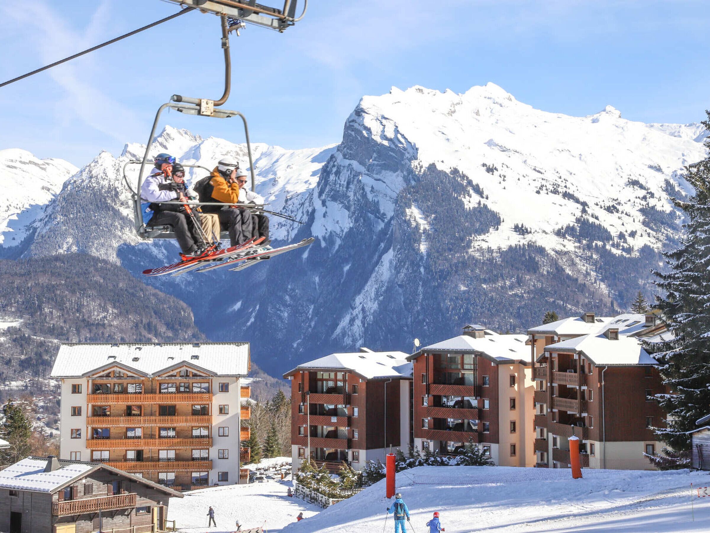 A ski lift with skiers, a mountain backdrop, and a ski resort building with balconies.