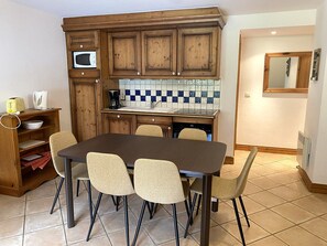 Een keuken met houten kasten, een betegelde spatwand, een magnetron, een koffiezetapparaat en een eettafel met stoelen.