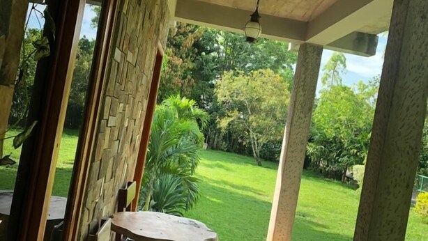 Un espacio de estar al aire libre cubierto, con pared de piedra y vistas a un jardín cuidado.