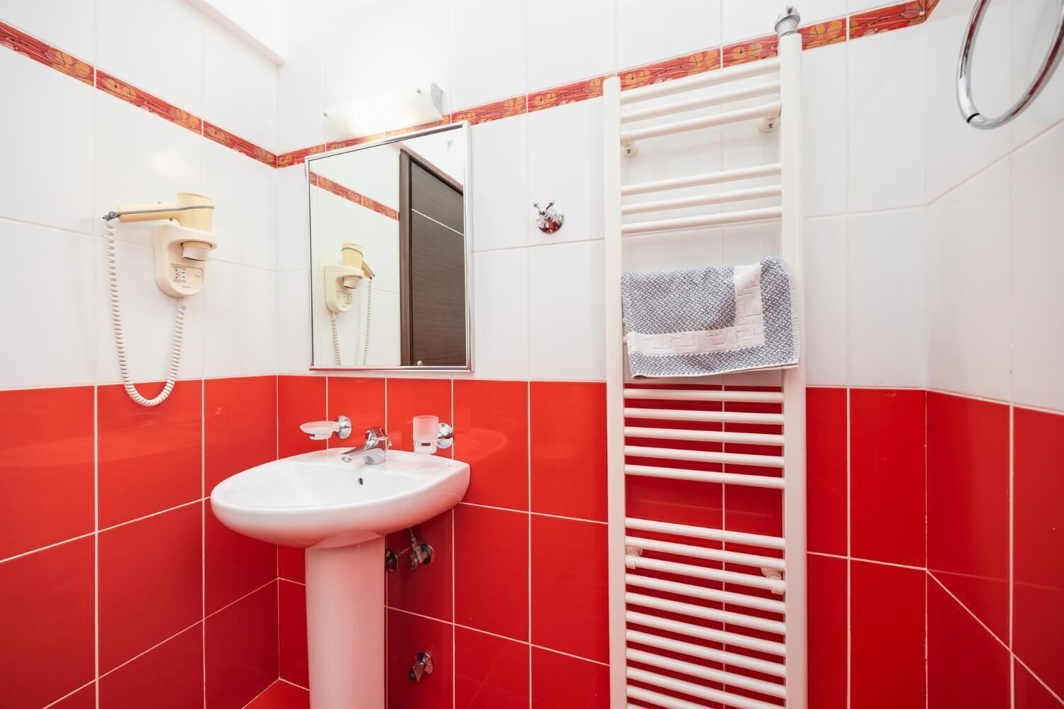Un bany amb un lavabo blanc, rajoles vermelles, un mirall, un penjallotxes i un telèfon.