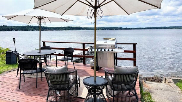 An outdoor deck with a grill, tables, chairs, and umbrellas overlooking a body of water. - Saratoga Lakeside Retreat #3 (Saratoga Springs)