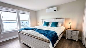 A bedroom with a wooden bed, two bedside tables, a nightstand, and a window with a view of the water. - Saratoga Lakeside Retreat #3 (Saratoga Springs)