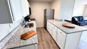 A compact kitchen with white cabinets, a stainless steel sink, a built-in refrigerator, and a wooden cutting board on the countertop. - Saratoga Lakeside Retreat #3 (Saratoga Springs)