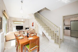 Eine moderne Küche mit einem Edelstahl-Kühlschrank, einem Essbereich mit einem Holztisch und Stühlen sowie einer Treppe mit Glastrennwand.