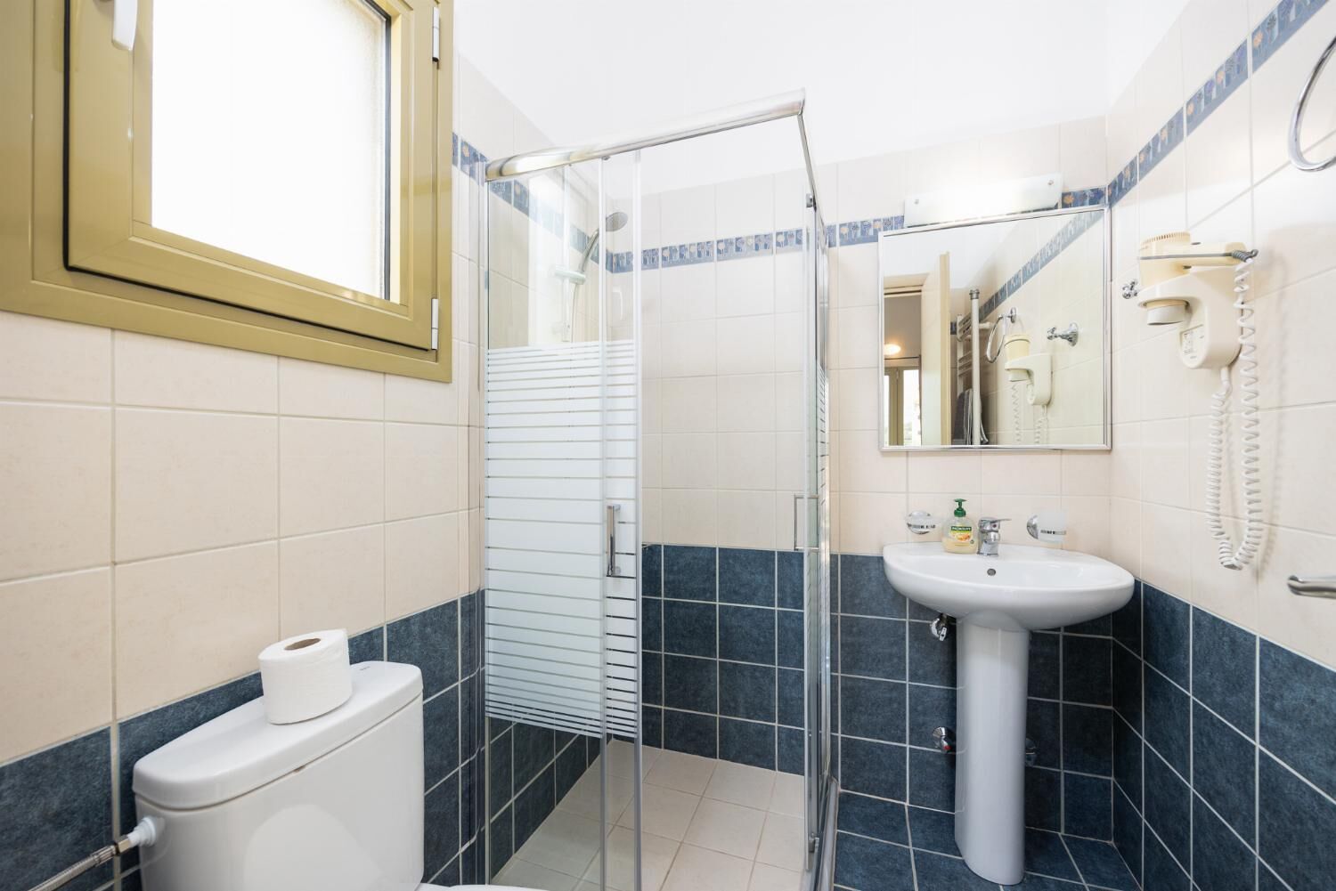 Un baño con inodoro, ducha con puerta de cristal, lavamanos y espejo.