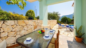 Un comedor con pared de piedra, una mesa dispuesta con platos azules y blancos, y vistas a una piscina y montañas.