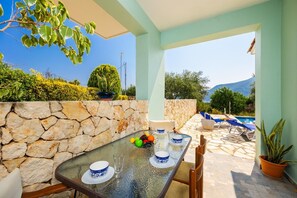 A dining area with a stone wall, a table set with blue and white plates, and a view of a pool and mountains.