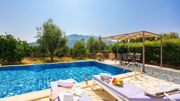 Zona de piscina con sillones de descanso, un pérgola y vistas a las montañas.