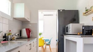 Una cocina moderna con armarios blancos, un refrigerador negro y un microondas. Hay una ventana que proporciona luz natural y una puerta que da a otra habitación.