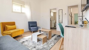 Una sala moderna con un sofá amarillo, un sillón azul, un sofá gris, una mesa de centro de madera y un mueble de madera claro.