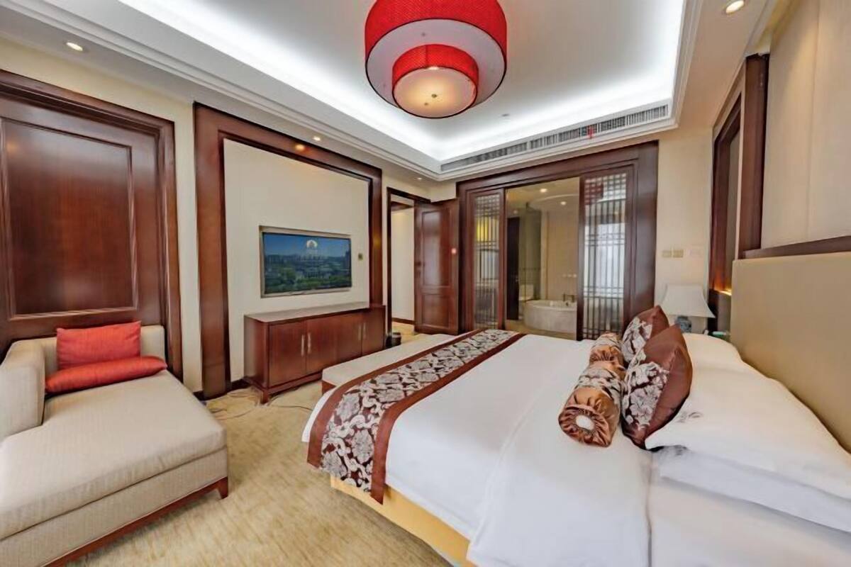 Quarto de hotel com uma cama grande, um sofá, uma escrivaninha e um quadro na parede.