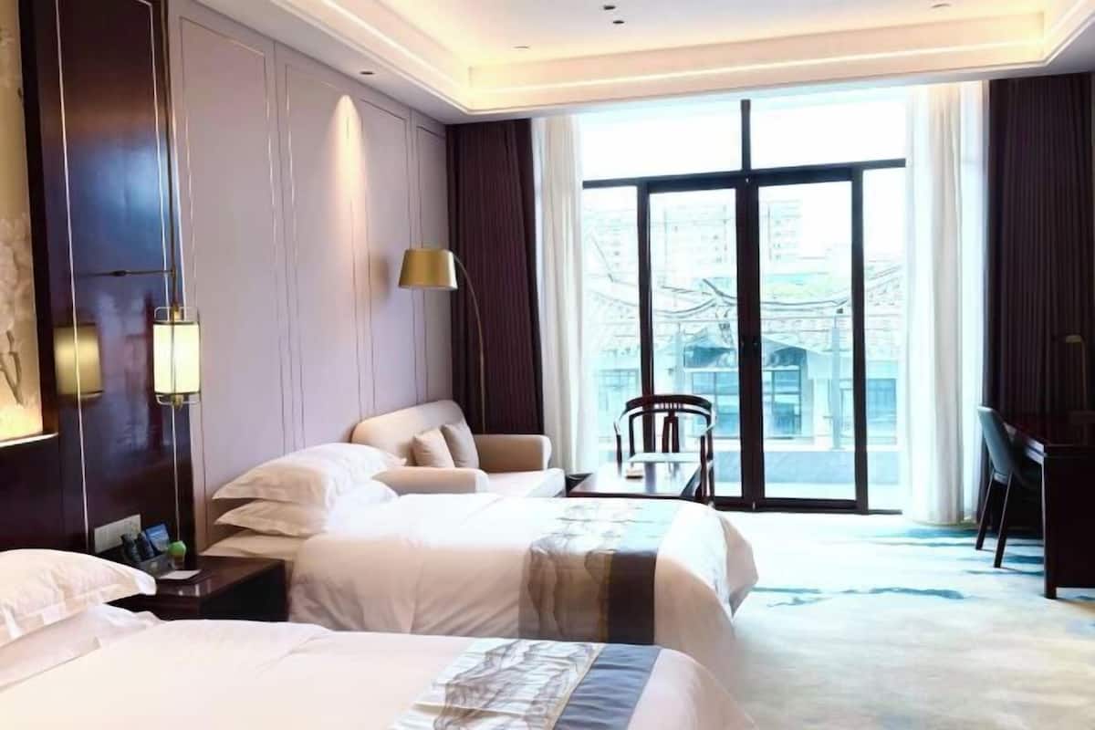 Ein Hotelzimmer mit zwei Betten, einem Schreibtisch, einem Stuhl und einem groĂen Fenster.