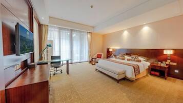 Een hotelkamer met een groot bed, een bureau met stoel, een televisie en een raam met gordijnen.