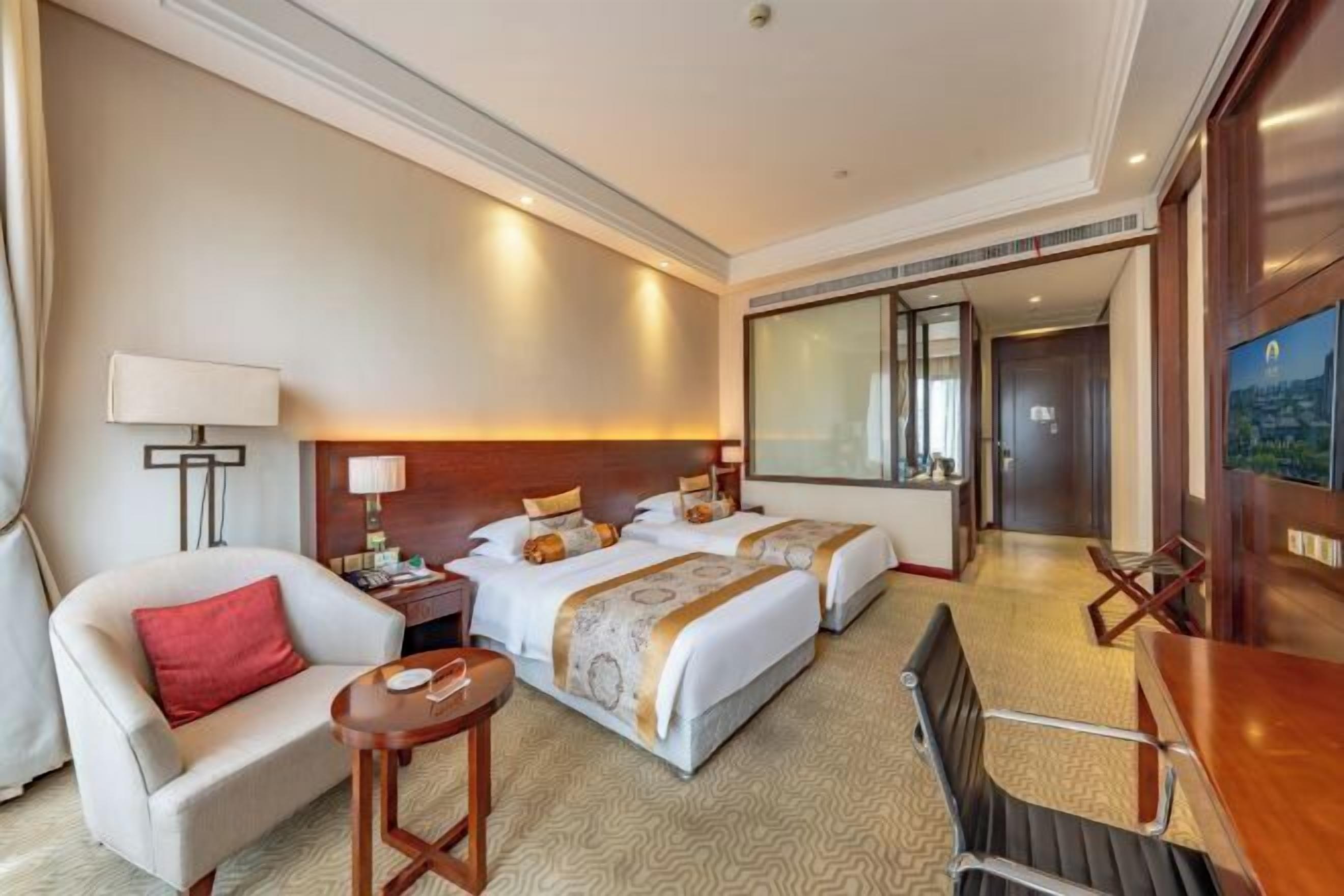 A hotel room with two beds, a desk, a chair, a lamp, and a large mirror.