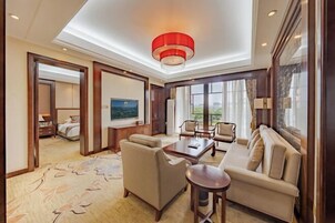 Habitación de hotel con sofá, sillones, una mesita de centro, televisor y un ventanal con vista a la ciudad.