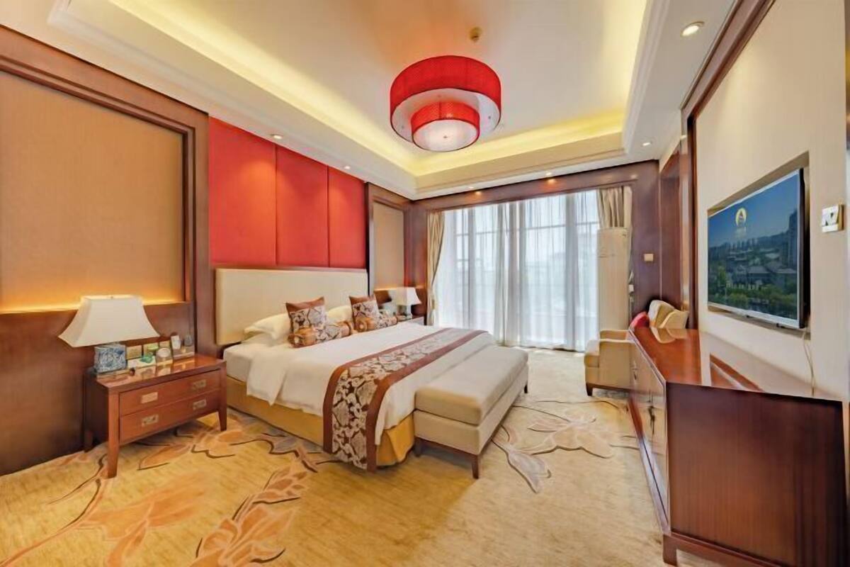 Quarto de hotel com uma cama grande, mesa de cabeceira, televisão e vista para o exterior.