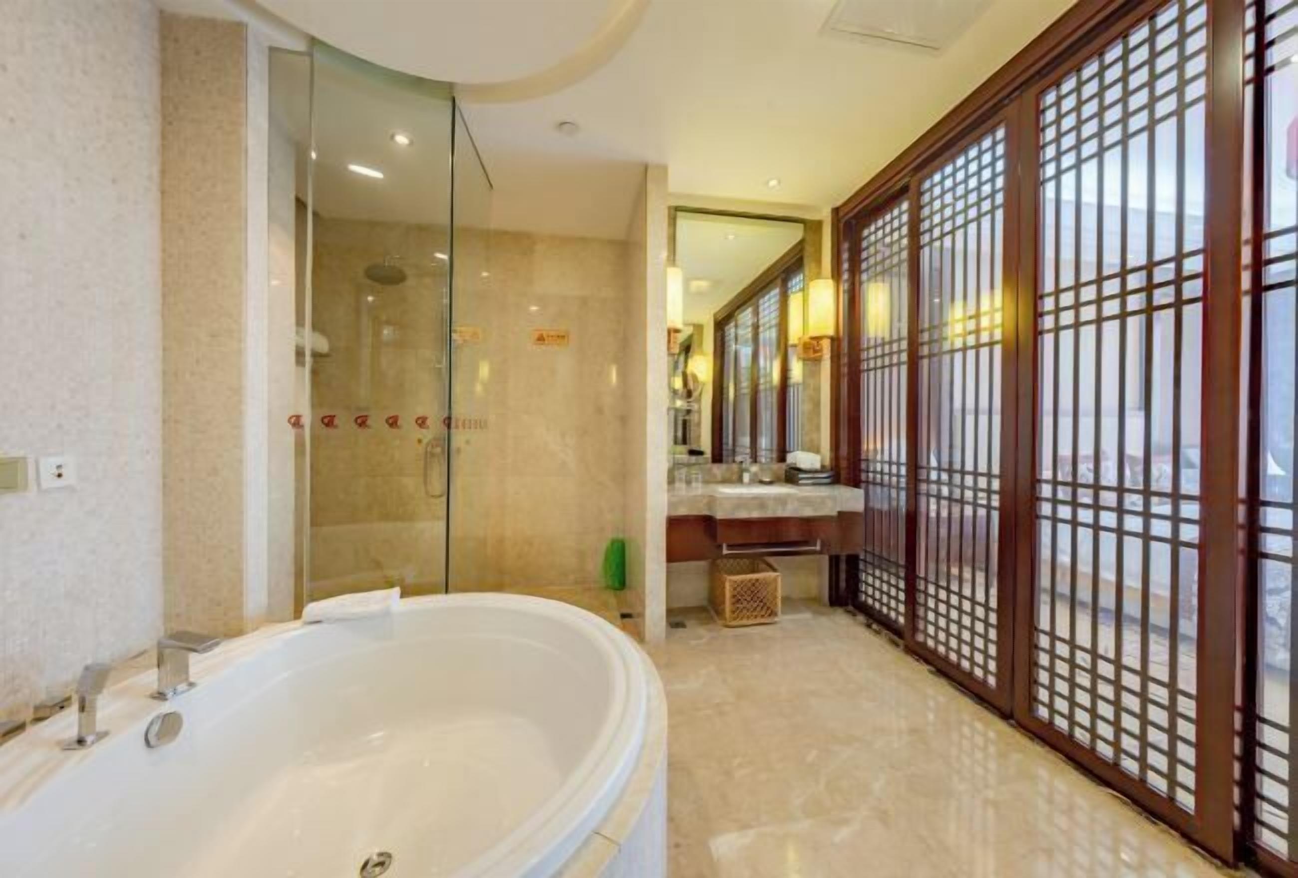A modern bathroom with a large bathtub, a glass shower enclosure, and a wooden partition with a grid design.