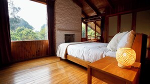 A wooden cabin bedroom with a bed, a nightstand, a lamp, and a view of the forest. - La Auxiliadora - Classic Mountain Chalet (Montecito)