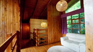 A wooden cabin interior with a white sofa, a woven light fixture, and a window with curtains. - La Auxiliadora - Classic Mountain Chalet (Montecito)