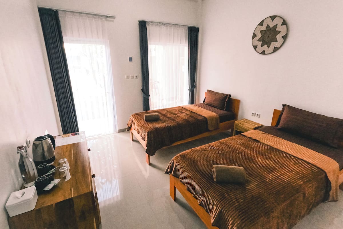 A hotel room with two single beds, a wooden desk with a kettle and cups, and a wall clock.