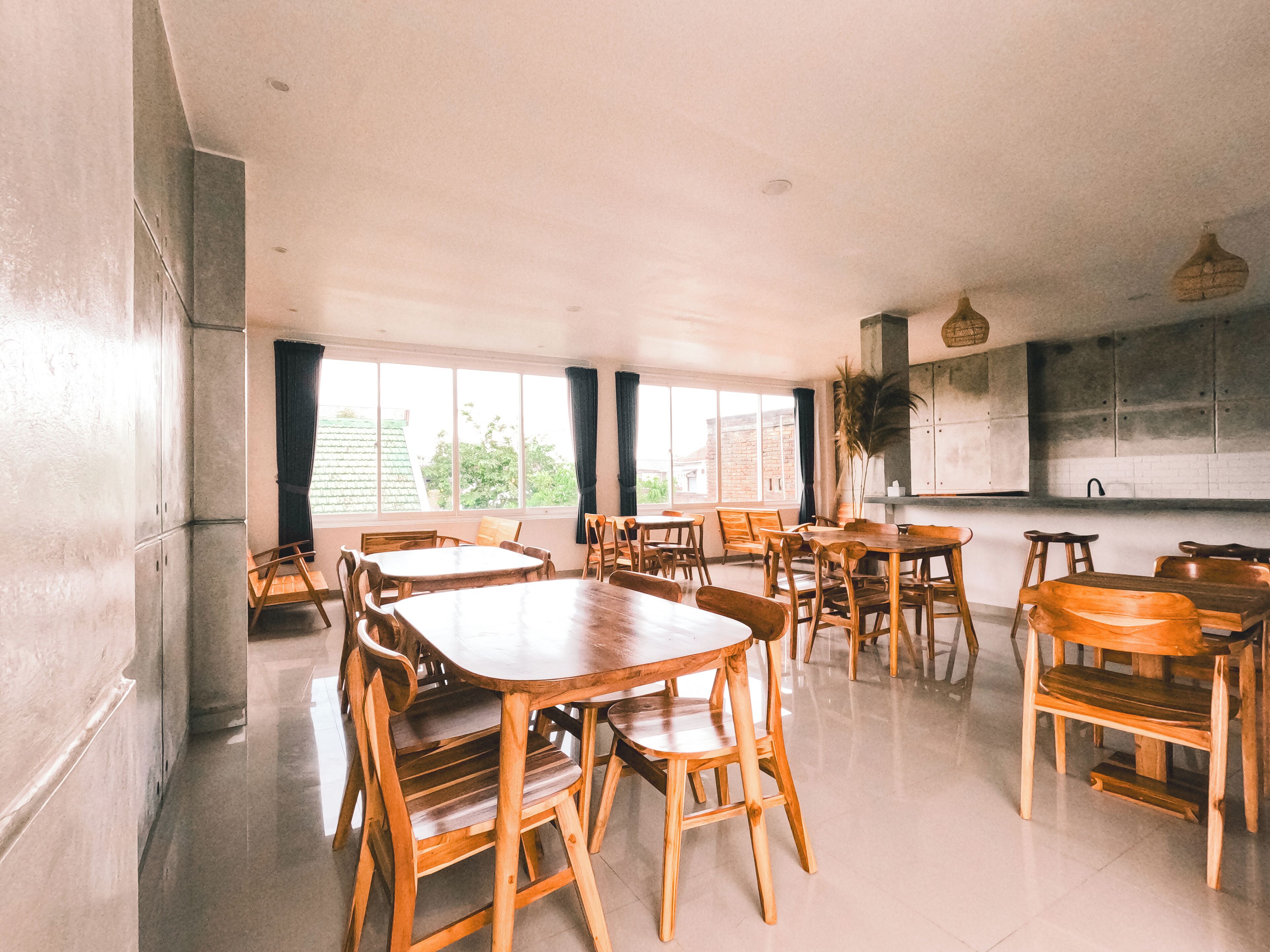 Un comedor espacioso con mesas y sillas de madera, ventanas amplias y una zona de cocina con armarios.