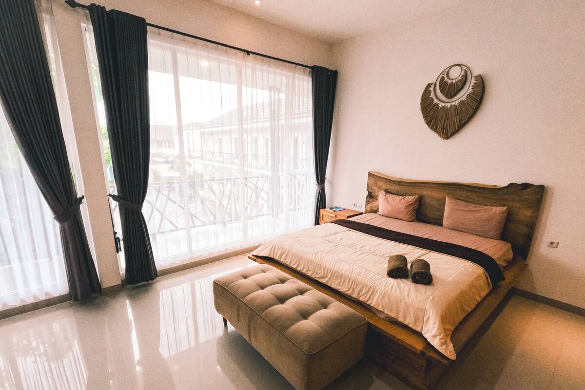 A bedroom with a large bed, a wooden headboard, a bench, and a wall-mounted decorative piece.