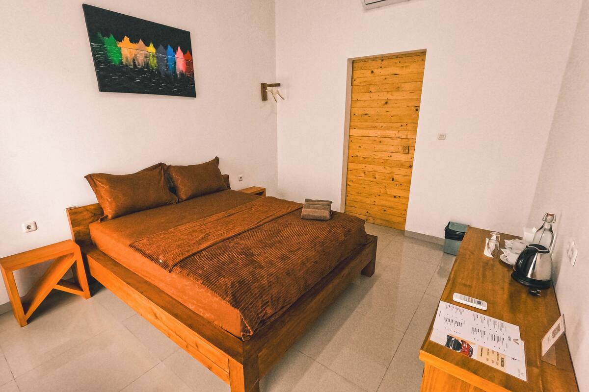 A bedroom with a wooden bed, a nightstand, a wooden door, and a small table with a kettle and a menu.