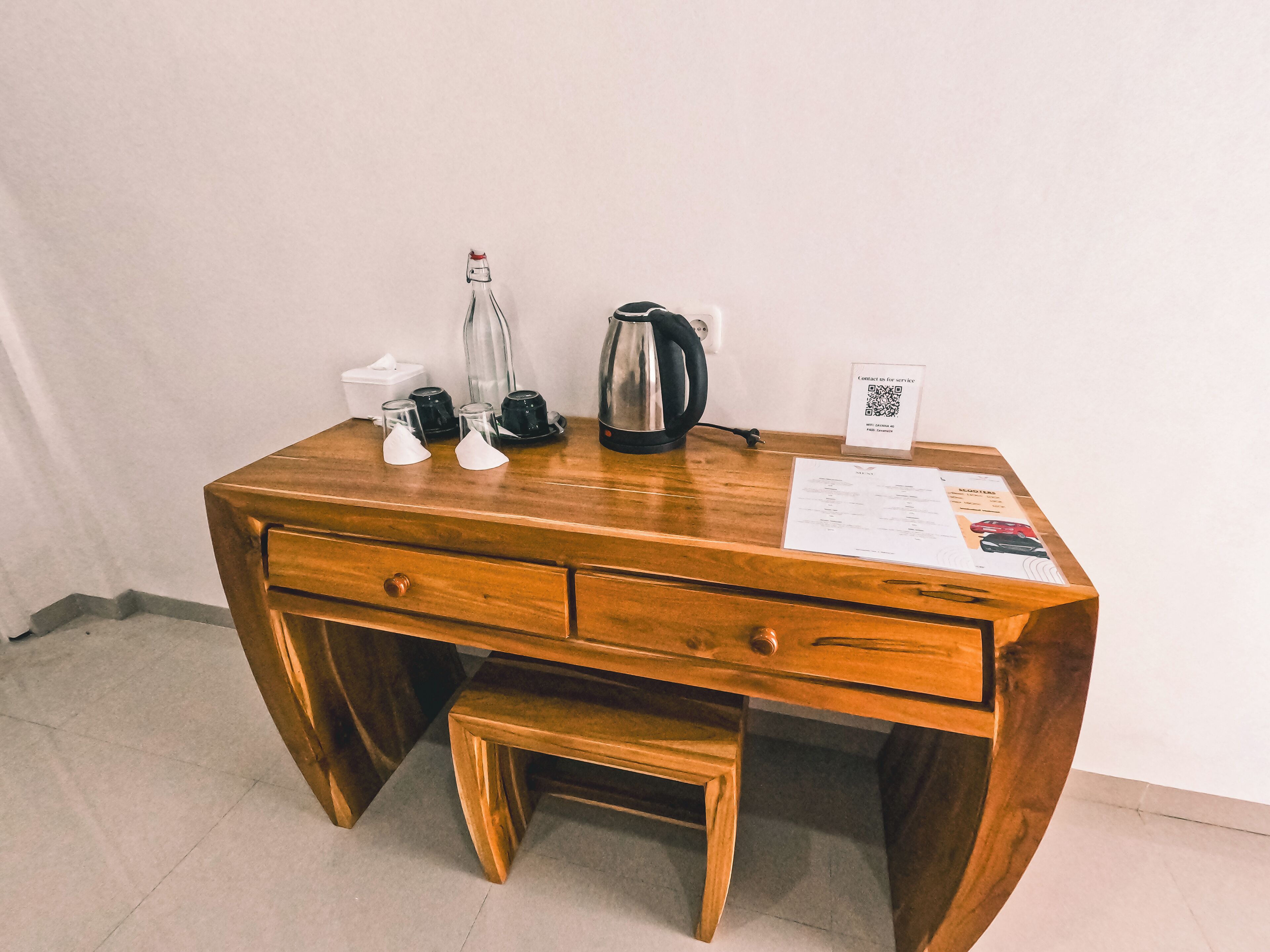 Un bureau en bois avec une bouilloire, une machine à café et un panneau avec un code QR.