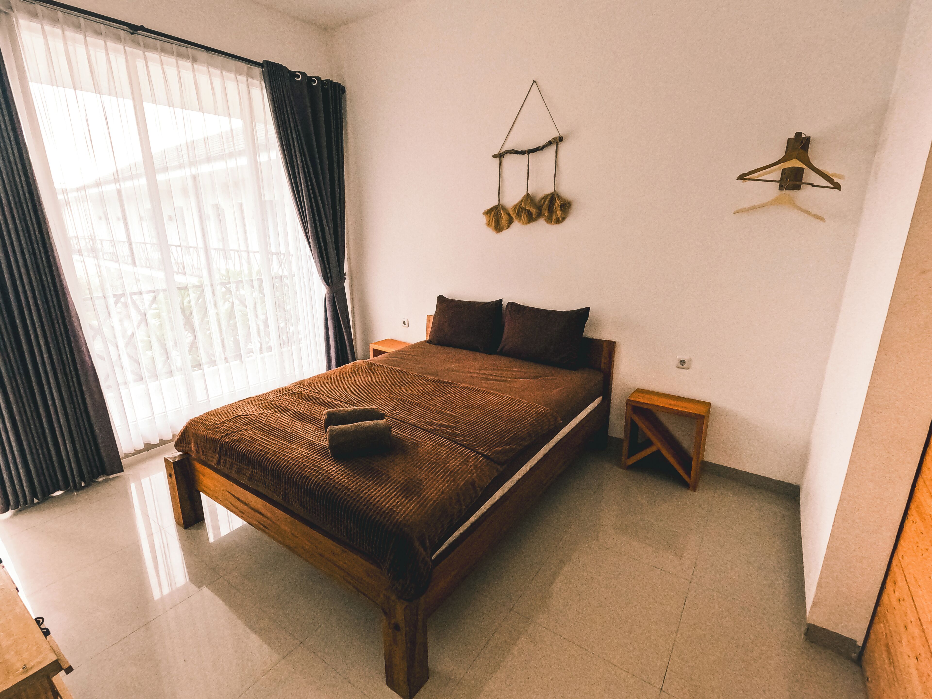 A spacious bedroom with a large bed, a wooden nightstand, a hanging light fixture, and a window with curtains.