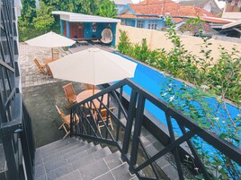 Una escalera conduce a una terraza con mobiliario exterior, piscina y vistas de los edificios circundantes.