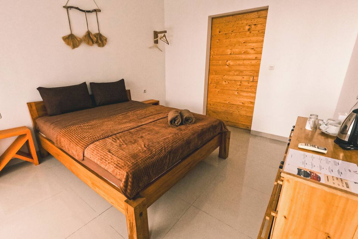 A wooden bed with a brown blanket, a wooden nightstand, and a wooden door.