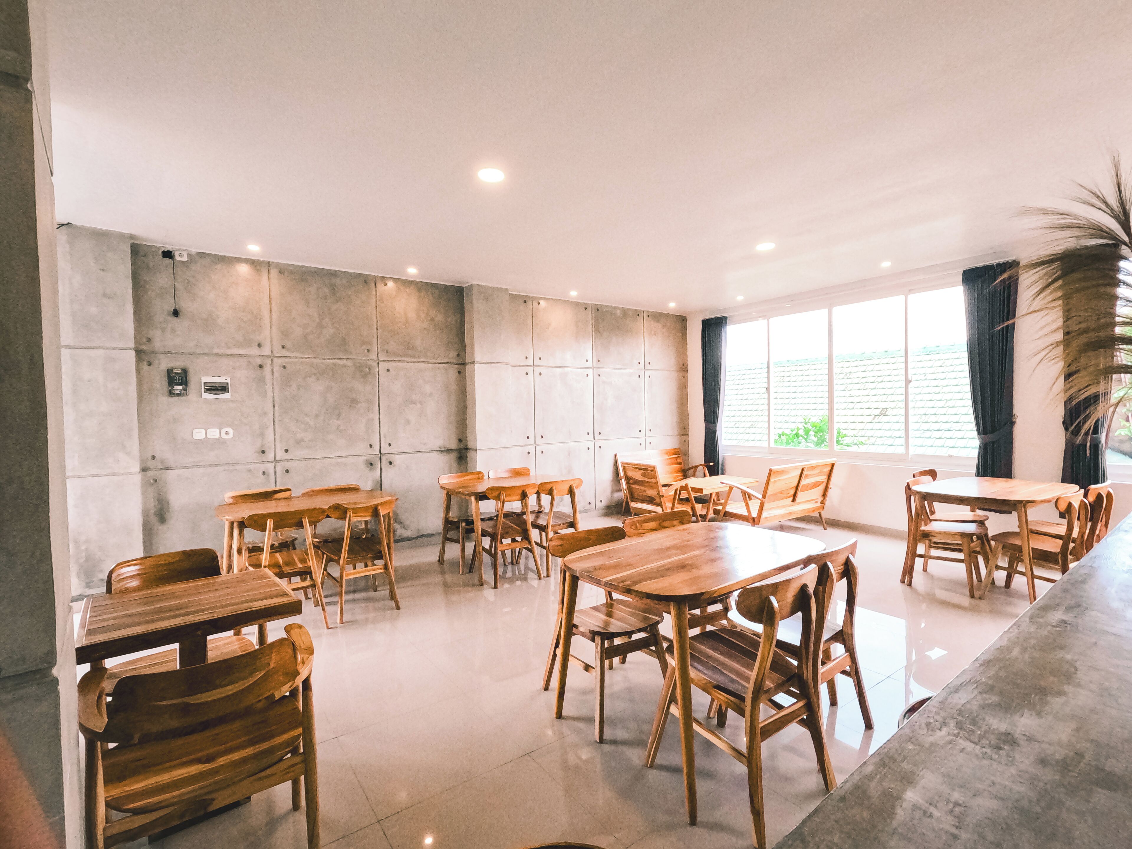 Une pièce spacieuse avec plusieurs tables et chaises en bois, une grande fenêtre avec des rideaux et un mur en béton équipé de prises électriques.
