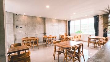 Une pièce spacieuse avec plusieurs tables et chaises en bois, une grande fenêtre avec des rideaux et un mur en béton équipé de prises électriques.