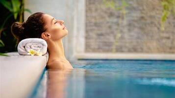 A person relaxing in a pool with a towel and flower on the edge.